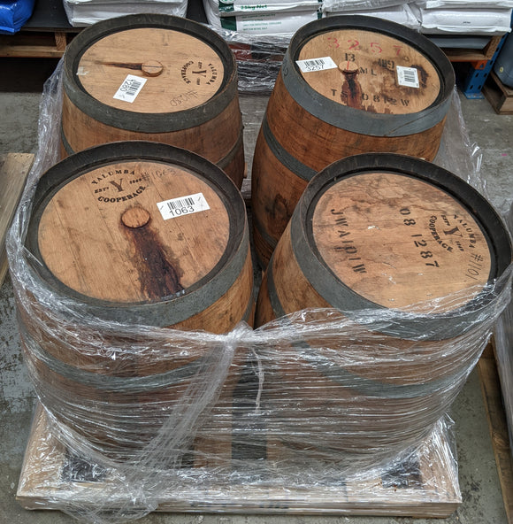 Four wooden barrels with visible branding and labels, wrapped in plastic on a pallet.