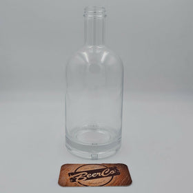 A clear glass bottle with a thick base and short neck, shown on a light gray background with a small wooden 'BeerCo' coaster in front of it.