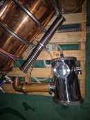 Copper and stainless steel still on a wooden pallet with hoses and pipes.