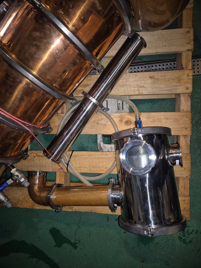 Copper and stainless steel still on a wooden pallet with hoses and pipes.