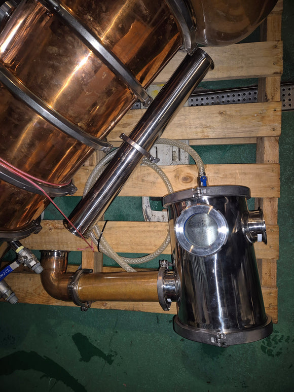 Copper and stainless steel still on a wooden pallet with hoses and pipes.