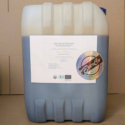 A large plastic drum labeled with the 'Best Ground' brand, containing organic raw 100% blue agave syrup.