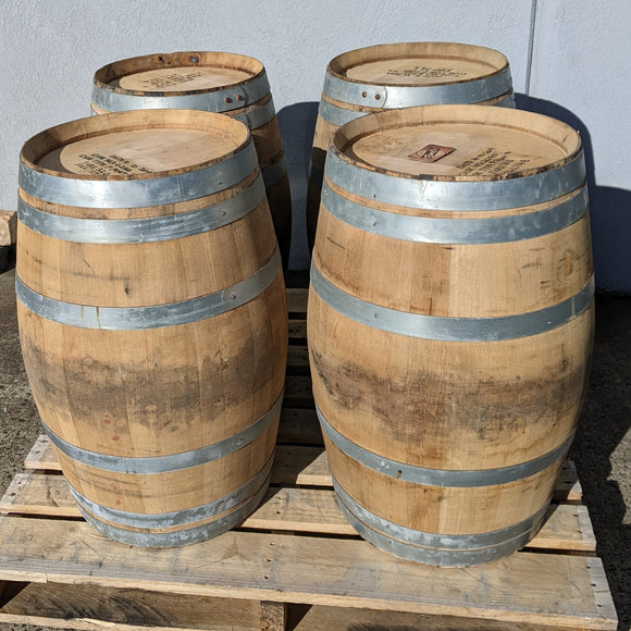 Four wooden barrels with metal bands on a wooden pallet against a gray background